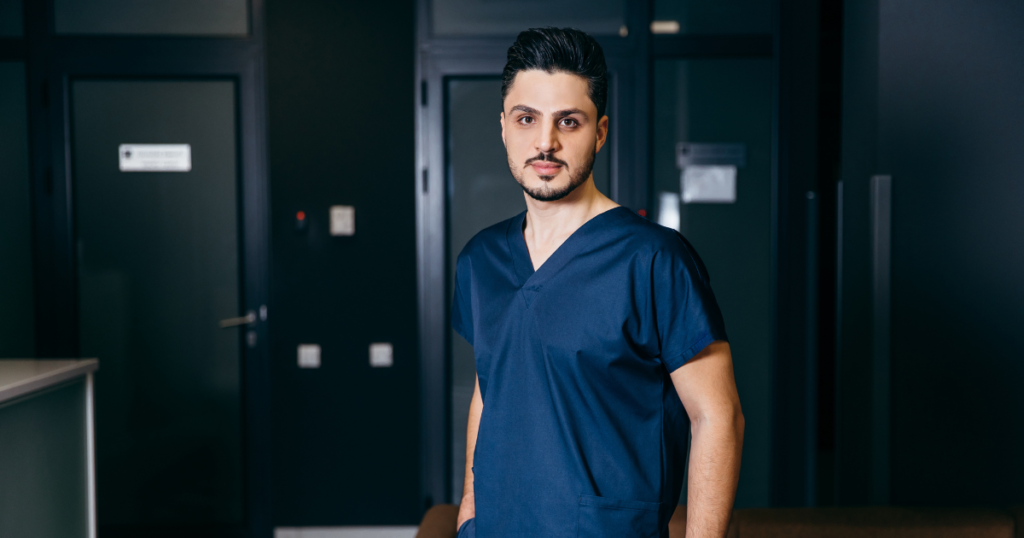 A professional healthcare worker in a modern setting wearing a navy-blue scrub uniform, standing confidently in a medical facility.